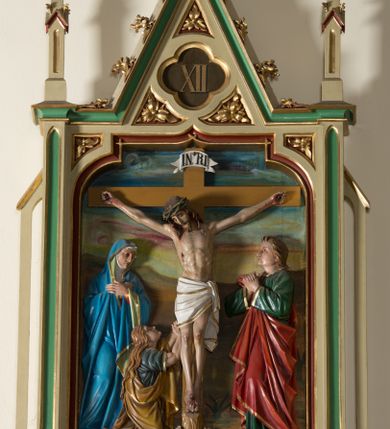 Zdjęcie nr 5: Czternaście płaskorzeźbionych, polichromowanych stacji drogi krzyżowej ukazanych na tle malowanego pejzażu. Przedstawienia ujęte w neogotyckie, architektoniczne ramy zamknięte wimpergą z żabkami, zwieńczoną  kwiatonem z krzyżem, pośrodku wimpergi czterolistna płycina z numerem stacji. Wnęka na płaskorzeźbę zamknięta łukiem dwuramiennym. Partia cokołowa ujęta od dołu podwieszeniem z rozetką. Polichromia ram w odcieniu kremowym, zielonym i ciemnoczerwonym z pozłacanym detalem. Sceny wielofigurowe z Chrystusem w centrum. Chrystus na większości przedstawień jest ubrany w długą, białą tunikę z pozłacaną lamówką i czerwony płaszcz z błękitną podszewką. Twarz owalna okolona ciemnymi włosami i ciemnym zarostem. W tle pejzaż z elementami architektury. Na stacji pierwszej, w prawym dolnym rogu napis „Ferd(inand) Stuflesser / Bildabauer / S(ank)t Ulrich Gröden Tirol / 1903”.