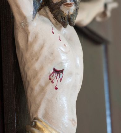 Zdjęcie nr 3: Pełnoplastyczna, polichromowana figura Chrystusa przybita do krzyża trzema gwoździami. Sylwetka zmarłego Chrystusa smukła, wychudła o naturalnej karnacji z lekko zaznaczoną muskulaturą i układem kostnym klatki piersiowej. Ramiona uniesione wysoko tworzą łuk, dłonie z wyprostowanymi palcami wskazującym i środkowym, nogi ugięte w kolanach. Głowa lekko pochylona, zwrócona w prawą stronę. Twarz podłużna, oczy zamknięte, nos długi, broda krótka rozdzielona na końcu w dwa pukle. Głowę okalają długie, kręcone włosy opadające na ramiona. Perizonium krótkie, ciasto oplatające biodra, spięte na lewym boku. Z boku, dłoni, stóp i spod korony cierniowej spływają strużki krwi. Polichromia ciała naturalistyczna. Krzyż gładki, prosty, pomalowany na ciemnobrązowy kolor. Nad głową barokowy titulus w formie kartusza z owalną płyciną w polu z napisem „INRI”, dekorowany ornamentem małżowinowo-chrząstkowym. Polichromia w odsłoniętych partiach ciała naturalistyczna.
