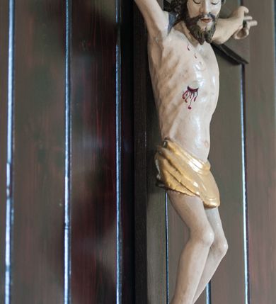 Zdjęcie nr 2: Pełnoplastyczna, polichromowana figura Chrystusa przybita do krzyża trzema gwoździami. Sylwetka zmarłego Chrystusa smukła, wychudła o naturalnej karnacji z lekko zaznaczoną muskulaturą i układem kostnym klatki piersiowej. Ramiona uniesione wysoko tworzą łuk, dłonie z wyprostowanymi palcami wskazującym i środkowym, nogi ugięte w kolanach. Głowa lekko pochylona, zwrócona w prawą stronę. Twarz podłużna, oczy zamknięte, nos długi, broda krótka rozdzielona na końcu w dwa pukle. Głowę okalają długie, kręcone włosy opadające na ramiona. Perizonium krótkie, ciasto oplatające biodra, spięte na lewym boku. Z boku, dłoni, stóp i spod korony cierniowej spływają strużki krwi. Polichromia ciała naturalistyczna. Krzyż gładki, prosty, pomalowany na ciemnobrązowy kolor. Nad głową barokowy titulus w formie kartusza z owalną płyciną w polu z napisem „INRI”, dekorowany ornamentem małżowinowo-chrząstkowym. Polichromia w odsłoniętych partiach ciała naturalistyczna.
