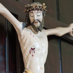 Zdjęcie nr 1: Pełnoplastyczna, polichromowana figura Chrystusa przybita do krzyża trzema gwoździami. Sylwetka zmarłego Chrystusa smukła, wychudła o naturalnej karnacji z lekko zaznaczoną muskulaturą i układem kostnym klatki piersiowej. Ramiona uniesione wysoko tworzą łuk, dłonie z wyprostowanymi palcami wskazującym i środkowym, nogi ugięte w kolanach. Głowa lekko pochylona, zwrócona w prawą stronę. Twarz podłużna, oczy zamknięte, nos długi, broda krótka rozdzielona na końcu w dwa pukle. Głowę okalają długie, kręcone włosy opadające na ramiona. Perizonium krótkie, ciasto oplatające biodra, spięte na lewym boku. Z boku, dłoni, stóp i spod korony cierniowej spływają strużki krwi. Polichromia ciała naturalistyczna. Krzyż gładki, prosty, pomalowany na ciemnobrązowy kolor. Nad głową barokowy titulus w formie kartusza z owalną płyciną w polu z napisem „INRI”, dekorowany ornamentem małżowinowo-chrząstkowym. Polichromia w odsłoniętych partiach ciała naturalistyczna.
