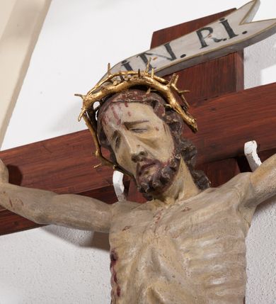 Zdjęcie nr 2: Pełnoplastyczna, drążona od tyłu, polichromowana figura Chrystusa przybita do prostego krzyża trzema gwoździami. Sylwetka zmarłego Chrystusa smukła z wyraźnie zaznaczoną muskulaturą i głębokim wcięciem w talii i widocznym układem kostnym klatki piersiowej. Ramiona uniesione wysoko tworzą łuk, dłonie o wyprostowanych palcach. Nogi znacznie ugięte w kolanach, założone prawa na lewą. Głowa pochylona, lekko zwrócona w prawą stronę. Na głowie Chrystus ma założoną pozłacaną koronę cierniową. Twarz podłużna z zapadniętymi policzkami, oczy zamknięte z opadłymi kącikami i ściągniętymi brwiami, nos długi o prostym profilu, usta małe i zamknięte. Włosy długie, opadające na kark, broda krótka i kręcona. Perizonium długie, sięgające połowy łydki, po bokach opadające swobodnie kaskadowymi fałdami. Polichromowane na kolor szary, na brzegu złocone. Nad głową titulus w formie poziomej banderoli z napisem „I.N.R.I.”. W odsłoniętych partiach ciała figura polichromowana naturalistycznie o ciemnej karnacji z zaznaczonymi śladami męki. Krzyż szeroki, prosty, pokryty bejcą. 

