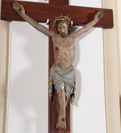 Zdjęcie nr 1: Pełnoplastyczna, drążona od tyłu, polichromowana figura Chrystusa przybita do prostego krzyża trzema gwoździami. Sylwetka zmarłego Chrystusa smukła z wyraźnie zaznaczoną muskulaturą i głębokim wcięciem w talii i widocznym układem kostnym klatki piersiowej. Ramiona uniesione wysoko tworzą łuk, dłonie o wyprostowanych palcach. Nogi znacznie ugięte w kolanach, założone prawa na lewą. Głowa pochylona, lekko zwrócona w prawą stronę. Na głowie Chrystus ma założoną pozłacaną koronę cierniową. Twarz podłużna z zapadniętymi policzkami, oczy zamknięte z opadłymi kącikami i ściągniętymi brwiami, nos długi o prostym profilu, usta małe i zamknięte. Włosy długie, opadające na kark, broda krótka i kręcona. Perizonium długie, sięgające połowy łydki, po bokach opadające swobodnie kaskadowymi fałdami. Polichromowane na kolor szary, na brzegu złocone. Nad głową titulus w formie poziomej banderoli z napisem „I.N.R.I.”. W odsłoniętych partiach ciała figura polichromowana naturalistycznie o ciemnej karnacji z zaznaczonymi śladami męki. Krzyż szeroki, prosty, pokryty bejcą. 
