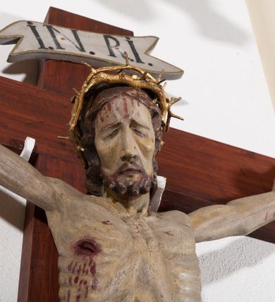 Zdjęcie nr 3: Pełnoplastyczna, drążona od tyłu, polichromowana figura Chrystusa przybita do prostego krzyża trzema gwoździami. Sylwetka zmarłego Chrystusa smukła z wyraźnie zaznaczoną muskulaturą i głębokim wcięciem w talii i widocznym układem kostnym klatki piersiowej. Ramiona uniesione wysoko tworzą łuk, dłonie o wyprostowanych palcach. Nogi znacznie ugięte w kolanach, założone prawa na lewą. Głowa pochylona, lekko zwrócona w prawą stronę. Na głowie Chrystus ma założoną pozłacaną koronę cierniową. Twarz podłużna z zapadniętymi policzkami, oczy zamknięte z opadłymi kącikami i ściągniętymi brwiami, nos długi o prostym profilu, usta małe i zamknięte. Włosy długie, opadające na kark, broda krótka i kręcona. Perizonium długie, sięgające połowy łydki, po bokach opadające swobodnie kaskadowymi fałdami. Polichromowane na kolor szary, na brzegu złocone. Nad głową titulus w formie poziomej banderoli z napisem „I.N.R.I.”. W odsłoniętych partiach ciała figura polichromowana naturalistycznie o ciemnej karnacji z zaznaczonymi śladami męki. Krzyż szeroki, prosty, pokryty bejcą. 
