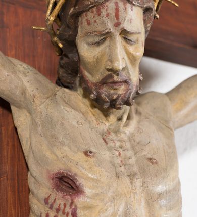 Zdjęcie nr 4: Pełnoplastyczna, drążona od tyłu, polichromowana figura Chrystusa przybita do prostego krzyża trzema gwoździami. Sylwetka zmarłego Chrystusa smukła z wyraźnie zaznaczoną muskulaturą i głębokim wcięciem w talii i widocznym układem kostnym klatki piersiowej. Ramiona uniesione wysoko tworzą łuk, dłonie o wyprostowanych palcach. Nogi znacznie ugięte w kolanach, założone prawa na lewą. Głowa pochylona, lekko zwrócona w prawą stronę. Na głowie Chrystus ma założoną pozłacaną koronę cierniową. Twarz podłużna z zapadniętymi policzkami, oczy zamknięte z opadłymi kącikami i ściągniętymi brwiami, nos długi o prostym profilu, usta małe i zamknięte. Włosy długie, opadające na kark, broda krótka i kręcona. Perizonium długie, sięgające połowy łydki, po bokach opadające swobodnie kaskadowymi fałdami. Polichromowane na kolor szary, na brzegu złocone. Nad głową titulus w formie poziomej banderoli z napisem „I.N.R.I.”. W odsłoniętych partiach ciała figura polichromowana naturalistycznie o ciemnej karnacji z zaznaczonymi śladami męki. Krzyż szeroki, prosty, pokryty bejcą. 

