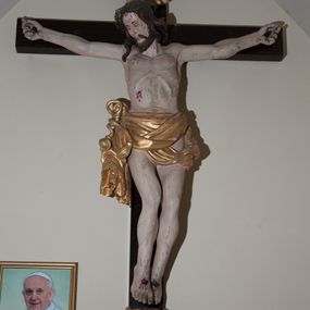 Zdjęcie nr 1: Rzeźba Chrystusa przybita do krzyża czterema gwoździami, ukazana w typie Cristo morte. Ciało o szeroko rozstawionych ramionach, sylwetka szczupła, choć muskularna. Chrystus ma głowę przechyloną na prawe ramię. Twarz szczupła, z wąskim i długim nosem, zamkniętymi oczami, na wpół otwartymi ustami, okolona krótką brodą. Włosy długie, ciemnobrązowe spływające na prawe ramię, na głowie zielona korona cierniowa. Perizonium złocone, zdobione na brzegu koronką, swobodnie oplatające biodra, przewiązane sznurem na prawym boku, z jednym końcem dłuższym, zwisającym wzdłuż prawego uda. Z boku, dłoni, stóp i spod korony cierniowej spływają strużki krwi. Polichromia ciała naturalistyczna. Krzyż gładki, prosty, pomalowany na ciemnobrązowy kolor; nad głową Chrystusa titulus z napisem „INRI” w języku łacińskim, greckim i hebrajskim. U podstawy pionowej belki krzyża złocona i marmoryzowana, wolutowo wygięta konsolka. 