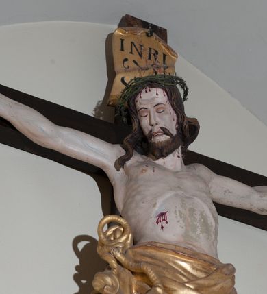Zdjęcie nr 2: Rzeźba Chrystusa przybita do krzyża czterema gwoździami, ukazana w typie Cristo morte. Ciało o szeroko rozstawionych ramionach, sylwetka szczupła, choć muskularna. Chrystus ma głowę przechyloną na prawe ramię. Twarz szczupła, z wąskim i długim nosem, zamkniętymi oczami, na wpół otwartymi ustami, okolona krótką brodą. Włosy długie, ciemnobrązowe spływające na prawe ramię, na głowie zielona korona cierniowa. Perizonium złocone, zdobione na brzegu koronką, swobodnie oplatające biodra, przewiązane sznurem na prawym boku, z jednym końcem dłuższym, zwisającym wzdłuż prawego uda. Z boku, dłoni, stóp i spod korony cierniowej spływają strużki krwi. Polichromia ciała naturalistyczna. Krzyż gładki, prosty, pomalowany na ciemnobrązowy kolor; nad głową Chrystusa titulus z napisem „INRI” w języku łacińskim, greckim i hebrajskim. U podstawy pionowej belki krzyża złocona i marmoryzowana, wolutowo wygięta konsolka. 