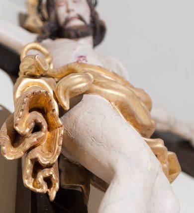 Zdjęcie nr 3: Rzeźba Chrystusa przybita do krzyża czterema gwoździami, ukazana w typie Cristo morte. Ciało o szeroko rozstawionych ramionach, sylwetka szczupła, choć muskularna. Chrystus ma głowę przechyloną na prawe ramię. Twarz szczupła, z wąskim i długim nosem, zamkniętymi oczami, na wpół otwartymi ustami, okolona krótką brodą. Włosy długie, ciemnobrązowe spływające na prawe ramię, na głowie zielona korona cierniowa. Perizonium złocone, zdobione na brzegu koronką, swobodnie oplatające biodra, przewiązane sznurem na prawym boku, z jednym końcem dłuższym, zwisającym wzdłuż prawego uda. Z boku, dłoni, stóp i spod korony cierniowej spływają strużki krwi. Polichromia ciała naturalistyczna. Krzyż gładki, prosty, pomalowany na ciemnobrązowy kolor; nad głową Chrystusa titulus z napisem „INRI” w języku łacińskim, greckim i hebrajskim. U podstawy pionowej belki krzyża złocona i marmoryzowana, wolutowo wygięta konsolka. 