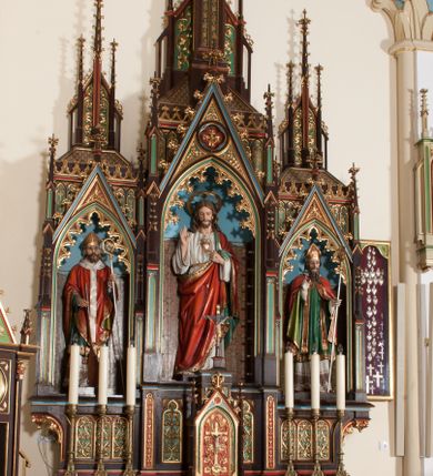 Zdjęcie nr 4: Nastawa ołtarzowa architektoniczna, jednokondygnacyjna, trójosiowa z marmurowym portatylem. Mensa drewniana, prostopadłościenna, na niewielkim cokole. Antepedium płaskorzeźbione, polichromowane, artykułowane dwiema złoconymi kolumienkami. W centrum kwadratowa płycina, w polu której czwórliść ze złoconym krzyżem. Po bokach dwie płaskorzeźbione, kwadratowe płyciny, przedzielone na pół, w każdej maswerk z bogatą dekoracją floralną. Całość zwieńczona wydatnym profilowanym gzymsem. Tabernakulum w formie prostopadłościennej skrzynki, ustawionej na niskim cokole, flankowane dwoma filarami ustawionymi ukośnie i zakończonymi pinaklami. Zwieńczenie tabernakulum w formie prostopadłościennego przyczółka, na którym ustawiony jest krucyfiks. Drzwiczki tabernakulum w kształcie ostrołukowej arkady, w polu której płaskorzeźbiony krucyfiks na tle wici roślinnej utworzonej z kłosów zbóż i winnej latorośli. Retabulum umieszczone na cokole. Predella trójosiowa, zdobiona rzędem pseudomaswerków. Osie kondygnacji flankowane pilastrami z pinaklami zakończonymi kwiatonami. W środkowej osi ostrołukowa nisza zwieńczona wimpergą mieszcząca rzeźbę Najświętszego Serca Pana Jezusa. W osiach bocznych, w analogicznych niszach zwieńczonych wimpergami rzeźby: po lewej św. Wojciecha, po prawej św. Stanisława. Zwieńczenie w formie trzech wieżyczek z pinaklami, kwiatonami i żabkami, część środkowa, najwyższa. Struktura malowana na ciemny brąz, wypełnienia płycin zielone, czerwone i błękitne. Partie ornamentu oraz detale architektoniczne złocone. Ornamentyka neogotycka wypełnia każdą wolną przestrzeń ołtarza: trójliście, maswerki, czołganki etc.

