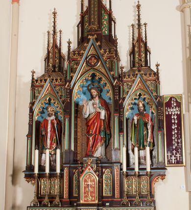 Zdjęcie nr 3: Nastawa ołtarzowa architektoniczna, jednokondygnacyjna, trójosiowa z marmurowym portatylem. Mensa drewniana, prostopadłościenna, na niewielkim cokole. Antepedium płaskorzeźbione, polichromowane, artykułowane dwiema złoconymi kolumienkami. W centrum kwadratowa płycina, w polu której czwórliść ze złoconym krzyżem. Po bokach dwie płaskorzeźbione, kwadratowe płyciny, przedzielone na pół, w każdej maswerk z bogatą dekoracją floralną. Całość zwieńczona wydatnym profilowanym gzymsem. Tabernakulum w formie prostopadłościennej skrzynki, ustawionej na niskim cokole, flankowane dwoma filarami ustawionymi ukośnie i zakończonymi pinaklami. Zwieńczenie tabernakulum w formie prostopadłościennego przyczółka, na którym ustawiony jest krucyfiks. Drzwiczki tabernakulum w kształcie ostrołukowej arkady, w polu której płaskorzeźbiony krucyfiks na tle wici roślinnej utworzonej z kłosów zbóż i winnej latorośli. Retabulum umieszczone na cokole. Predella trójosiowa, zdobiona rzędem pseudomaswerków. Osie kondygnacji flankowane pilastrami z pinaklami zakończonymi kwiatonami. W środkowej osi ostrołukowa nisza zwieńczona wimpergą mieszcząca rzeźbę Najświętszego Serca Pana Jezusa. W osiach bocznych, w analogicznych niszach zwieńczonych wimpergami rzeźby: po lewej św. Wojciecha, po prawej św. Stanisława. Zwieńczenie w formie trzech wieżyczek z pinaklami, kwiatonami i żabkami, część środkowa, najwyższa. Struktura malowana na ciemny brąz, wypełnienia płycin zielone, czerwone i błękitne. Partie ornamentu oraz detale architektoniczne złocone. Ornamentyka neogotycka wypełnia każdą wolną przestrzeń ołtarza: trójliście, maswerki, czołganki etc.

