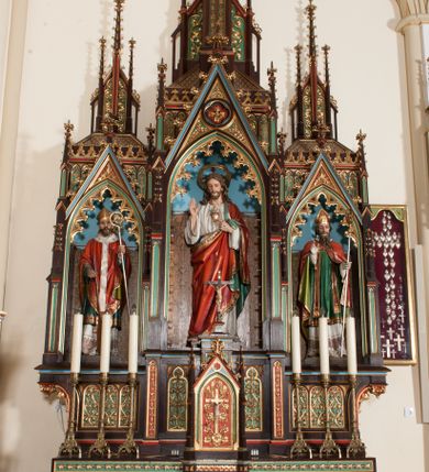 Zdjęcie nr 1: Nastawa ołtarzowa architektoniczna, jednokondygnacyjna, trójosiowa z marmurowym portatylem. Mensa drewniana, prostopadłościenna, na niewielkim cokole. Antepedium płaskorzeźbione, polichromowane, artykułowane dwiema złoconymi kolumienkami. W centrum kwadratowa płycina, w polu której czwórliść ze złoconym krzyżem. Po bokach dwie płaskorzeźbione, kwadratowe płyciny, przedzielone na pół, w każdej maswerk z bogatą dekoracją floralną. Całość zwieńczona wydatnym profilowanym gzymsem. Tabernakulum w formie prostopadłościennej skrzynki, ustawionej na niskim cokole, flankowane dwoma filarami ustawionymi ukośnie i zakończonymi pinaklami. Zwieńczenie tabernakulum w formie prostopadłościennego przyczółka, na którym ustawiony jest krucyfiks. Drzwiczki tabernakulum w kształcie ostrołukowej arkady, w polu której płaskorzeźbiony krucyfiks na tle wici roślinnej utworzonej z kłosów zbóż i winnej latorośli. Retabulum umieszczone na cokole. Predella trójosiowa, zdobiona rzędem pseudomaswerków. Osie kondygnacji flankowane pilastrami z pinaklami zakończonymi kwiatonami. W środkowej osi ostrołukowa nisza zwieńczona wimpergą mieszcząca rzeźbę Najświętszego Serca Pana Jezusa. W osiach bocznych, w analogicznych niszach zwieńczonych wimpergami rzeźby: po lewej św. Wojciecha, po prawej św. Stanisława. Zwieńczenie w formie trzech wieżyczek z pinaklami, kwiatonami i żabkami, część środkowa, najwyższa. Struktura malowana na ciemny brąz, wypełnienia płycin zielone, czerwone i błękitne. Partie ornamentu oraz detale architektoniczne złocone. Ornamentyka neogotycka wypełnia każdą wolną przestrzeń ołtarza: trójliście, maswerki, czołganki etc.

