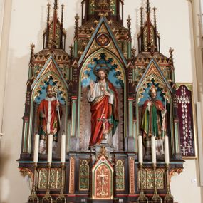Zdjęcie nr 1: Nastawa ołtarzowa architektoniczna, jednokondygnacyjna, trójosiowa z marmurowym portatylem. Mensa drewniana, prostopadłościenna, na niewielkim cokole. Antepedium płaskorzeźbione, polichromowane, artykułowane dwiema złoconymi kolumienkami. W centrum kwadratowa płycina, w polu której czwórliść ze złoconym krzyżem. Po bokach dwie płaskorzeźbione, kwadratowe płyciny, przedzielone na pół, w każdej maswerk z bogatą dekoracją floralną. Całość zwieńczona wydatnym profilowanym gzymsem. Tabernakulum w formie prostopadłościennej skrzynki, ustawionej na niskim cokole, flankowane dwoma filarami ustawionymi ukośnie i zakończonymi pinaklami. Zwieńczenie tabernakulum w formie prostopadłościennego przyczółka, na którym ustawiony jest krucyfiks. Drzwiczki tabernakulum w kształcie ostrołukowej arkady, w polu której płaskorzeźbiony krucyfiks na tle wici roślinnej utworzonej z kłosów zbóż i winnej latorośli. Retabulum umieszczone na cokole. Predella trójosiowa, zdobiona rzędem pseudomaswerków. Osie kondygnacji flankowane pilastrami z pinaklami zakończonymi kwiatonami. W środkowej osi ostrołukowa nisza zwieńczona wimpergą mieszcząca rzeźbę Najświętszego Serca Pana Jezusa. W osiach bocznych, w analogicznych niszach zwieńczonych wimpergami rzeźby: po lewej św. Wojciecha, po prawej św. Stanisława. Zwieńczenie w formie trzech wieżyczek z pinaklami, kwiatonami i żabkami, część środkowa, najwyższa. Struktura malowana na ciemny brąz, wypełnienia płycin zielone, czerwone i błękitne. Partie ornamentu oraz detale architektoniczne złocone. Ornamentyka neogotycka wypełnia każdą wolną przestrzeń ołtarza: trójliście, maswerki, czołganki etc.

