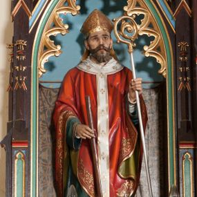 Zdjęcie nr 1: Rzeźba pełnoplastyczna, ustawiona na niskim cokole. Święty ukazany w pozycji stojącej, frontalnie, z wiosłem w prawej dłoni i pastorałem w lewej. Twarz podłużna, z długim i wąskim nosem, wzrokiem skierowanym ku górze, okolona średniej długości brodą. Święty ubrany jest w długą, białą albę, dekorowaną u dołu geometrycznymi wzorami, zieloną rokietę, czerwony ornat z oliwkowo-zieloną podszewką, biały paliusz i złotą infułę na głowie. Wszystkie szaty dekorowane są na brzegach złoconą dekoracją ornamentalną. Polichromia w odsłoniętych partiach ciała naturalistyczna.