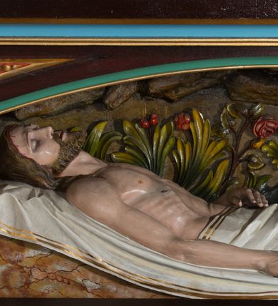 Zdjęcie nr 1: Figura umieszczona w mensie ołtarza bocznego, w niszy w formie leżącego prostokąta zamkniętego obniżonym łukiem koszowym, od przodu ujętej w profilowaną ramę. Chrystus leżący na plecach, ułożony na białych tkaninach, widoczny z prawego profilu. Głowa Jezusa lekko opada na prawe ramię; twarz pociągła, oczy zamknięte, nos prosty, lekko uchylone, wąskie usta. Twarz okolona zarostem, włosy długie, spod których widoczne strugi krwi. Prawa ręka ułożona wzdłuż ciała, lewa złożona na pasie. Lewa noga lekko ugięta, prawa wyprostowana. Nogi przykryte białym materiałem ze złotą lamówką, tors nagi. Widoczne ślady męki, polichromia w odsłoniętych partiach ciała naturalistyczna. Za Chrystusem płaskorzeźbione tło z bujną roślinnością i skałami.