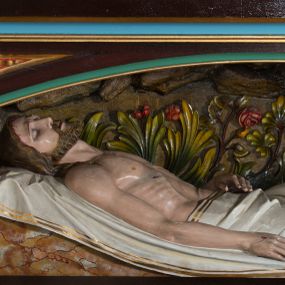 Zdjęcie nr 1: Figura umieszczona w mensie ołtarza bocznego, w niszy w formie leżącego prostokąta zamkniętego obniżonym łukiem koszowym, od przodu ujętej w profilowaną ramę. Chrystus leżący na plecach, ułożony na białych tkaninach, widoczny z prawego profilu. Głowa Jezusa lekko opada na prawe ramię; twarz pociągła, oczy zamknięte, nos prosty, lekko uchylone, wąskie usta. Twarz okolona zarostem, włosy długie, spod których widoczne strugi krwi. Prawa ręka ułożona wzdłuż ciała, lewa złożona na pasie. Lewa noga lekko ugięta, prawa wyprostowana. Nogi przykryte białym materiałem ze złotą lamówką, tors nagi. Widoczne ślady męki, polichromia w odsłoniętych partiach ciała naturalistyczna. Za Chrystusem płaskorzeźbione tło z bujną roślinnością i skałami.