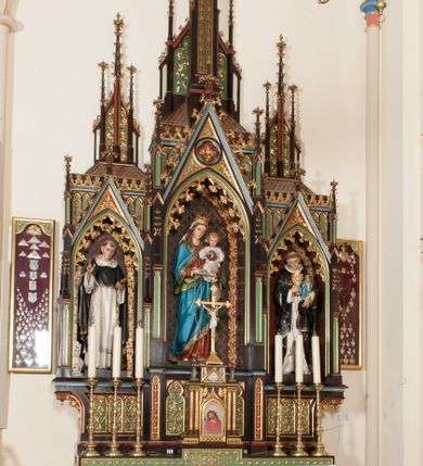 Zdjęcie nr 2: Nastawa ołtarzowa architektoniczna, jednokondygnacyjna, trójosiowa z marmurowym portatylem. Mensa drewniana, prostopadłościenna, na niewielkim cokole. Antepedium płaskorzeźbione, polichromowane, artykułowane dwiema złoconymi kolumienkami. W centrum kwadratowa płycina, w polu której czwórliść ze złoconym krzyżem. Po bokach dwie płaskorzeźbione, kwadratowe płyciny, przedzielone na pół, w każdej maswerk z bogatą dekoracją floralną. Całość zwieńczona wydatnym profilowanym gzymsem. Tabernakulum w formie prostopadłościennej skrzynki, ustawionej na niskim cokole, flankowane dwiema parami kolumn wspierających niepełne belkowanie z prostopadłościennym przyczółkiem, na którym ustawiony jest krucyfiks. Drzwiczki tabernakulum w kształcie ostrołukowej arkady, w polu której płaskorzeźbione przedstawienie Ecce Homo zredukowane do półpostaci Chrystusa w purpurowym płaszczu i koronie cierniowej; w przyłuczach drzwiczek kłosy zbóż i winna latorośl. W zwieńczeniu, na przyczółku monogram IHS, na osi kolumn dwa pinakle. Retabulum umieszczone na cokole. Predella trójosiowa, zdobiona rzędem pseudomaswerków. Osie kondygnacji flankowane pilastrami z pinaklami zwieńczonymi kwiatonami. W środkowej osi ostrołukowa nisza zwieńczona wimpergą mieszcząca rzeźbę Matki Boskiej z Dzieciątkiem. W osiach bocznych, w analogicznych niszach zwieńczonych wimpergami rzeźby: po lewej św. Dominika, po prawej św. Jacka. Zwieńczenie w formie trzech wieżyczek z pinaklami, zdobionymi kwiatonami i żabkami, część środkowa, najwyższa. Struktura malowana na ciemny brąz, wypełnienia płycin zielone, czerwone i błękitne. Partie ornamentu oraz detale architektoniczne złocone. Ornamentyka neogotycka wypełnia każdą wolną przestrzeń ołtarza: trójliście, maswerki, czołganki etc.
