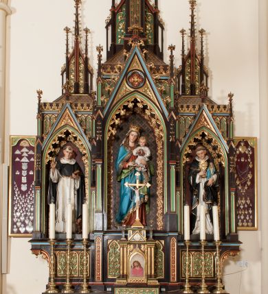 Zdjęcie nr 1: Nastawa ołtarzowa architektoniczna, jednokondygnacyjna, trójosiowa z marmurowym portatylem. Mensa drewniana, prostopadłościenna, na niewielkim cokole. Antepedium płaskorzeźbione, polichromowane, artykułowane dwiema złoconymi kolumienkami. W centrum kwadratowa płycina, w polu której czwórliść ze złoconym krzyżem. Po bokach dwie płaskorzeźbione, kwadratowe płyciny, przedzielone na pół, w każdej maswerk z bogatą dekoracją floralną. Całość zwieńczona wydatnym profilowanym gzymsem. Tabernakulum w formie prostopadłościennej skrzynki, ustawionej na niskim cokole, flankowane dwiema parami kolumn wspierających niepełne belkowanie z prostopadłościennym przyczółkiem, na którym ustawiony jest krucyfiks. Drzwiczki tabernakulum w kształcie ostrołukowej arkady, w polu której płaskorzeźbione przedstawienie Ecce Homo zredukowane do półpostaci Chrystusa w purpurowym płaszczu i koronie cierniowej; w przyłuczach drzwiczek kłosy zbóż i winna latorośl. W zwieńczeniu, na przyczółku monogram IHS, na osi kolumn dwa pinakle. Retabulum umieszczone na cokole. Predella trójosiowa, zdobiona rzędem pseudomaswerków. Osie kondygnacji flankowane pilastrami z pinaklami zwieńczonymi kwiatonami. W środkowej osi ostrołukowa nisza zwieńczona wimpergą mieszcząca rzeźbę Matki Boskiej z Dzieciątkiem. W osiach bocznych, w analogicznych niszach zwieńczonych wimpergami rzeźby: po lewej św. Dominika, po prawej św. Jacka. Zwieńczenie w formie trzech wieżyczek z pinaklami, zdobionymi kwiatonami i żabkami, część środkowa, najwyższa. Struktura malowana na ciemny brąz, wypełnienia płycin zielone, czerwone i błękitne. Partie ornamentu oraz detale architektoniczne złocone. Ornamentyka neogotycka wypełnia każdą wolną przestrzeń ołtarza: trójliście, maswerki, czołganki etc.

