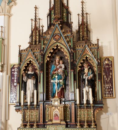 Zdjęcie nr 3: Nastawa ołtarzowa architektoniczna, jednokondygnacyjna, trójosiowa z marmurowym portatylem. Mensa drewniana, prostopadłościenna, na niewielkim cokole. Antepedium płaskorzeźbione, polichromowane, artykułowane dwiema złoconymi kolumienkami. W centrum kwadratowa płycina, w polu której czwórliść ze złoconym krzyżem. Po bokach dwie płaskorzeźbione, kwadratowe płyciny, przedzielone na pół, w każdej maswerk z bogatą dekoracją floralną. Całość zwieńczona wydatnym profilowanym gzymsem. Tabernakulum w formie prostopadłościennej skrzynki, ustawionej na niskim cokole, flankowane dwiema parami kolumn wspierających niepełne belkowanie z prostopadłościennym przyczółkiem, na którym ustawiony jest krucyfiks. Drzwiczki tabernakulum w kształcie ostrołukowej arkady, w polu której płaskorzeźbione przedstawienie Ecce Homo zredukowane do półpostaci Chrystusa w purpurowym płaszczu i koronie cierniowej; w przyłuczach drzwiczek kłosy zbóż i winna latorośl. W zwieńczeniu, na przyczółku monogram IHS, na osi kolumn dwa pinakle. Retabulum umieszczone na cokole. Predella trójosiowa, zdobiona rzędem pseudomaswerków. Osie kondygnacji flankowane pilastrami z pinaklami zwieńczonymi kwiatonami. W środkowej osi ostrołukowa nisza zwieńczona wimpergą mieszcząca rzeźbę Matki Boskiej z Dzieciątkiem. W osiach bocznych, w analogicznych niszach zwieńczonych wimpergami rzeźby: po lewej św. Dominika, po prawej św. Jacka. Zwieńczenie w formie trzech wieżyczek z pinaklami, zdobionymi kwiatonami i żabkami, część środkowa, najwyższa. Struktura malowana na ciemny brąz, wypełnienia płycin zielone, czerwone i błękitne. Partie ornamentu oraz detale architektoniczne złocone. Ornamentyka neogotycka wypełnia każdą wolną przestrzeń ołtarza: trójliście, maswerki, czołganki etc.
