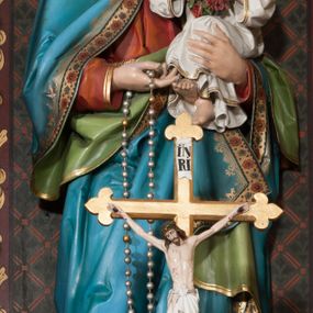Zdjęcie nr 1: Rzeźba pełnoplastyczna, ustawiona na niskim cokole, w delikatnym kontrapoście. Matka Boska trzyma na lewym ręku Dzieciątko Jezus, w prawej różaniec, a głowę delikatnie przechyla na lewą stronę. Ma owalną twarz, przymknięte oczy ze wzrokiem skierowanym w dół, długi i prosty nos oraz zarumienione policzki. Długie, brązowe włosy opadają grubymi lokami na plecy i ramiona. Maria ubrana jest w długą, czerwoną suknię z długimi rękawami oraz błękitny płaszcz z zieloną podszewką, spięty na piersiach złotą broszą, na głowie ma biały welon i koronę w typie otwartym. Szaty, a zwłaszcza płaszcz obwiedzione są złoconą lamówką i dekorowane ornamentalnym pasem. Dzieciątko ukazane jest w pozycji siedzącej, zwrócone trzy czwarte w prawo, w dłoniach trzyma wianek z czerwonych róż. Ma idealizowane rysy twarzy oraz krótkie, jasne i kędzierzawe włosy. Ubrane jest w długą, białą sukienkę z długimi rękawami. Polichromia w odsłoniętych partiach ciała naturalistyczna. 

