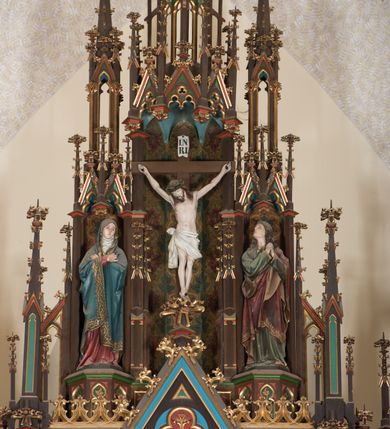 Zdjęcie nr 5: Ołtarz przyścienny, architektoniczny, trójosiowy, jednokondygnacyjny ze zwieńczeniem. Mensa drewniana, prostopadłościenna, na niewielkim cokole. Antepedium płaskorzeźbione, polichromowane, artykułowane złoconymi kolumienkami, zdwojonymi w skrajnych osiach. W centrum prostokątna płycina, w polu której  medalion ze złoconym krzyżem. Po bokach dwie płaskorzeźbione, polichromowane sceny Ofiara Izaaka (z lewej) i Ofiara Melchizedeka (z prawej). Całość zwieńczona wydatnym profilowanym gzymsem. Tabernakulum architektoniczne, trójosiowe z tronem wystawienia. Drzwiczki dekorowane kutą i odlewaną dekoracją w formie ostrołukowych maswerków oraz liter Alfa i Omega. Powyżej głęboka ostrołukowa nisza mieszcząca tron wystawienia. W osiach bocznych pełnoplastyczne, polichromowane figury klęczących aniołów w niszach zwieńczonych ażurowymi baldachimami. Poniżej trójlistne płyciny mieszczące płaskorzeźbione symbole: gołębica Ducha Świętego na tle glorii oraz skrzyżowane klucze i godło zakonu franciszkanów. Retabulum umieszczone na wysokim cokole o licu dekorowanym płaskorzeźbioną dekoracją pseudomaswerkową. Predella na cokole, z dwoma płaskorzeźbionymi, polichromowanymi scenami: Przekazanie kluczy św. Piotrowi (z lewej), Powołanie św. Pawła (z prawej). Sceny flankowane zdwojonymi, złoconymi kolumienkami o roślinnych kapitelach i zwieńczone ażurowym, ostrołukowym baldachimem z motywem trójliścia, żabek i pinakli. W osi środkowej kondygnacji ostrołukowa nisza zwieńczona wimpergą mieszcząca obraz Matki Boskiej Nieustającej Pomocy podtrzymywany przez pełnoplastyczne figury klęczących aniołów. Ponad nim złocony monogram Marii oraz korona. Na zasuwie obraz św. Michała Archanioła. Nisza ujęta dwiema kolumnami ustawionymi na ośmiobocznych cokołach, których trzony zajmują figury: po lewej św. Alfons Maria Liguori (?), po prawej św. Franciszka Ksawerego. Nad rzeźbami wiszą ozdobne baldachimy, nad nimi pełne trzony kolumn z kapitelami, nad którymi ustawiona kolejna para rzeźb. Po lewej rzeźba św. Magdaleny de Pazzi, po prawej figura Matki Boskiej Niepokalanie Poczętej. Obie podpory zwieńczone pinaklami. W osiach bocznych ostrołukowe nisze zamknięte wimpergami mieszczące pełnoplastyczne, polichromowane figury św. Piotra (z lewej) i św. Pawła (z prawej).  Poniżej figur po dwie prostokątne płyciny z płaskorzeźbowymi symbolami i podpisami: gołębicy Ducha Świętego „CONFIRMATIO”, kielicha z krzyżem „BAPTISMUS”, gałązki oliwnej oraz dyscypliny „PENITENTIA” oraz naczynia  i gałązki róż „EXSTREMA UNCTIO”. W zwieńczeniach usytuowane pełnoplastyczne figury aniołów trzymających banderole z napisami: „Adoremus!". Pośrodku grupa rzeźbiarska Ukrzyżowanie z pełnoplastycznymi, polichromowanymi figurami Chrystusa oraz Marii i św. Jana Ewangelisty ustawionymi pod rozbudowanymi, ażurowymi baldachimami. Struktura malowana na ciemny brąz, wypełnienia płycin zielone, czerwone i błękitne. Partie ornamentu oraz detale architektoniczne złocone. Ornamentyka neogotycka wypełnia każdą wolną przestrzeń ołtarza: trójliście, maswerki, czołganki etc.