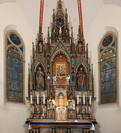 Zdjęcie nr 9: Ołtarz przyścienny, architektoniczny, trójosiowy, jednokondygnacyjny ze zwieńczeniem. Mensa drewniana, prostopadłościenna, na niewielkim cokole. Antepedium płaskorzeźbione, polichromowane, artykułowane złoconymi kolumienkami, zdwojonymi w skrajnych osiach. W centrum prostokątna płycina, w polu której  medalion ze złoconym krzyżem. Po bokach dwie płaskorzeźbione, polichromowane sceny Ofiara Izaaka (z lewej) i Ofiara Melchizedeka (z prawej). Całość zwieńczona wydatnym profilowanym gzymsem. Tabernakulum architektoniczne, trójosiowe z tronem wystawienia. Drzwiczki dekorowane kutą i odlewaną dekoracją w formie ostrołukowych maswerków oraz liter Alfa i Omega. Powyżej głęboka ostrołukowa nisza mieszcząca tron wystawienia. W osiach bocznych pełnoplastyczne, polichromowane figury klęczących aniołów w niszach zwieńczonych ażurowymi baldachimami. Poniżej trójlistne płyciny mieszczące płaskorzeźbione symbole: gołębica Ducha Świętego na tle glorii oraz skrzyżowane klucze i godło zakonu franciszkanów. Retabulum umieszczone na wysokim cokole o licu dekorowanym płaskorzeźbioną dekoracją pseudomaswerkową. Predella na cokole, z dwoma płaskorzeźbionymi, polichromowanymi scenami: Przekazanie kluczy św. Piotrowi (z lewej), Powołanie św. Pawła (z prawej). Sceny flankowane zdwojonymi, złoconymi kolumienkami o roślinnych kapitelach i zwieńczone ażurowym, ostrołukowym baldachimem z motywem trójliścia, żabek i pinakli. W osi środkowej kondygnacji ostrołukowa nisza zwieńczona wimpergą mieszcząca obraz Matki Boskiej Nieustającej Pomocy podtrzymywany przez pełnoplastyczne figury klęczących aniołów. Ponad nim złocony monogram Marii oraz korona. Na zasuwie obraz św. Michała Archanioła. Nisza ujęta dwiema kolumnami ustawionymi na ośmiobocznych cokołach, których trzony zajmują figury: po lewej św. Alfons Maria Liguori (?), po prawej św. Franciszka Ksawerego. Nad rzeźbami wiszą ozdobne baldachimy, nad nimi pełne trzony kolumn z kapitelami, nad którymi ustawiona kolejna para rzeźb. Po lewej rzeźba św. Magdaleny de Pazzi, po prawej figura Matki Boskiej Niepokalanie Poczętej. Obie podpory zwieńczone pinaklami. W osiach bocznych ostrołukowe nisze zamknięte wimpergami mieszczące pełnoplastyczne, polichromowane figury św. Piotra (z lewej) i św. Pawła (z prawej).  Poniżej figur po dwie prostokątne płyciny z płaskorzeźbowymi symbolami i podpisami: gołębicy Ducha Świętego „CONFIRMATIO”, kielicha z krzyżem „BAPTISMUS”, gałązki oliwnej oraz dyscypliny „PENITENTIA” oraz naczynia  i gałązki róż „EXSTREMA UNCTIO”. W zwieńczeniach usytuowane pełnoplastyczne figury aniołów trzymających banderole z napisami: „Adoremus!". Pośrodku grupa rzeźbiarska Ukrzyżowanie z pełnoplastycznymi, polichromowanymi figurami Chrystusa oraz Marii i św. Jana Ewangelisty ustawionymi pod rozbudowanymi, ażurowymi baldachimami. Struktura malowana na ciemny brąz, wypełnienia płycin zielone, czerwone i błękitne. Partie ornamentu oraz detale architektoniczne złocone. Ornamentyka neogotycka wypełnia każdą wolną przestrzeń ołtarza: trójliście, maswerki, czołganki etc.