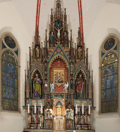 Zdjęcie nr 11: Ołtarz przyścienny, architektoniczny, trójosiowy, jednokondygnacyjny ze zwieńczeniem. Mensa drewniana, prostopadłościenna, na niewielkim cokole. Antepedium płaskorzeźbione, polichromowane, artykułowane złoconymi kolumienkami, zdwojonymi w skrajnych osiach. W centrum prostokątna płycina, w polu której  medalion ze złoconym krzyżem. Po bokach dwie płaskorzeźbione, polichromowane sceny Ofiara Izaaka (z lewej) i Ofiara Melchizedeka (z prawej). Całość zwieńczona wydatnym profilowanym gzymsem. Tabernakulum architektoniczne, trójosiowe z tronem wystawienia. Drzwiczki dekorowane kutą i odlewaną dekoracją w formie ostrołukowych maswerków oraz liter Alfa i Omega. Powyżej głęboka ostrołukowa nisza mieszcząca tron wystawienia. W osiach bocznych pełnoplastyczne, polichromowane figury klęczących aniołów w niszach zwieńczonych ażurowymi baldachimami. Poniżej trójlistne płyciny mieszczące płaskorzeźbione symbole: gołębica Ducha Świętego na tle glorii oraz skrzyżowane klucze i godło zakonu franciszkanów. Retabulum umieszczone na wysokim cokole o licu dekorowanym płaskorzeźbioną dekoracją pseudomaswerkową. Predella na cokole, z dwoma płaskorzeźbionymi, polichromowanymi scenami: Przekazanie kluczy św. Piotrowi (z lewej), Powołanie św. Pawła (z prawej). Sceny flankowane zdwojonymi, złoconymi kolumienkami o roślinnych kapitelach i zwieńczone ażurowym, ostrołukowym baldachimem z motywem trójliścia, żabek i pinakli. W osi środkowej kondygnacji ostrołukowa nisza zwieńczona wimpergą mieszcząca obraz Matki Boskiej Nieustającej Pomocy podtrzymywany przez pełnoplastyczne figury klęczących aniołów. Ponad nim złocony monogram Marii oraz korona. Na zasuwie obraz św. Michała Archanioła. Nisza ujęta dwiema kolumnami ustawionymi na ośmiobocznych cokołach, których trzony zajmują figury: po lewej św. Alfons Maria Liguori (?), po prawej św. Franciszka Ksawerego. Nad rzeźbami wiszą ozdobne baldachimy, nad nimi pełne trzony kolumn z kapitelami, nad którymi ustawiona kolejna para rzeźb. Po lewej rzeźba św. Magdaleny de Pazzi, po prawej figura Matki Boskiej Niepokalanie Poczętej. Obie podpory zwieńczone pinaklami. W osiach bocznych ostrołukowe nisze zamknięte wimpergami mieszczące pełnoplastyczne, polichromowane figury św. Piotra (z lewej) i św. Pawła (z prawej).  Poniżej figur po dwie prostokątne płyciny z płaskorzeźbowymi symbolami i podpisami: gołębicy Ducha Świętego „CONFIRMATIO”, kielicha z krzyżem „BAPTISMUS”, gałązki oliwnej oraz dyscypliny „PENITENTIA” oraz naczynia  i gałązki róż „EXSTREMA UNCTIO”. W zwieńczeniach usytuowane pełnoplastyczne figury aniołów trzymających banderole z napisami: „Adoremus!". Pośrodku grupa rzeźbiarska Ukrzyżowanie z pełnoplastycznymi, polichromowanymi figurami Chrystusa oraz Marii i św. Jana Ewangelisty ustawionymi pod rozbudowanymi, ażurowymi baldachimami. Struktura malowana na ciemny brąz, wypełnienia płycin zielone, czerwone i błękitne. Partie ornamentu oraz detale architektoniczne złocone. Ornamentyka neogotycka wypełnia każdą wolną przestrzeń ołtarza: trójliście, maswerki, czołganki etc.