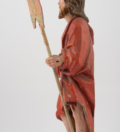 Zdjęcie nr 3: Rzeźba Chrystusa Zmartwychwstałego, ścięta z tyłu, ustawiona na niskim, zdwojonym, prostopadłościennym cokole. Chrystus ukazany  frontalnie, w kontrapoście, delikatnie przechylony w prawą stronę, w lewej ręce trzyma chorągiew zakończoną krzyżem, a prawą błogosławi. Twarz pociągła, długi i wąski nos, broda jasna, średniej długości. Włosy długie, brązowe, z przedziałkiem na środku głowy, opadają na ramiona w postaci loków, zasłaniając uszy. Chrystus ubrany jest w czerwony płaszcz, przewieszony przez lewe ramię, odsłaniający nagi tors.  Nimb krzyżowy w formie trzech wiązek promieni o nierównej długości. Polichromia naturalistyczna, nimb złocony.


