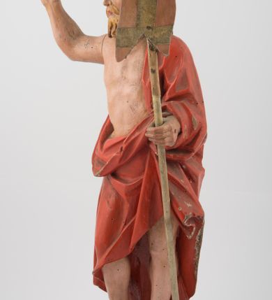 Zdjęcie nr 2: Rzeźba Chrystusa Zmartwychwstałego, ścięta z tyłu, ustawiona na niskim, zdwojonym, prostopadłościennym cokole. Chrystus ukazany  frontalnie, w kontrapoście, delikatnie przechylony w prawą stronę, w lewej ręce trzyma chorągiew zakończoną krzyżem, a prawą błogosławi. Twarz pociągła, długi i wąski nos, broda jasna, średniej długości. Włosy długie, brązowe, z przedziałkiem na środku głowy, opadają na ramiona w postaci loków, zasłaniając uszy. Chrystus ubrany jest w czerwony płaszcz, przewieszony przez lewe ramię, odsłaniający nagi tors.  Nimb krzyżowy w formie trzech wiązek promieni o nierównej długości. Polichromia naturalistyczna, nimb złocony.


