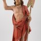 Zdjęcie nr 1: Rzeźba Chrystusa Zmartwychwstałego, ścięta z tyłu, ustawiona na niskim, zdwojonym, prostopadłościennym cokole. Chrystus ukazany  frontalnie, w kontrapoście, delikatnie przechylony w prawą stronę, w lewej ręce trzyma chorągiew zakończoną krzyżem, a prawą błogosławi. Twarz pociągła, długi i wąski nos, broda jasna, średniej długości. Włosy długie, brązowe, z przedziałkiem na środku głowy, opadają na ramiona w postaci loków, zasłaniając uszy. Chrystus ubrany jest w czerwony płaszcz, przewieszony przez lewe ramię, odsłaniający nagi tors.  Nimb krzyżowy w formie trzech wiązek promieni o nierównej długości. Polichromia naturalistyczna, nimb złocony.


