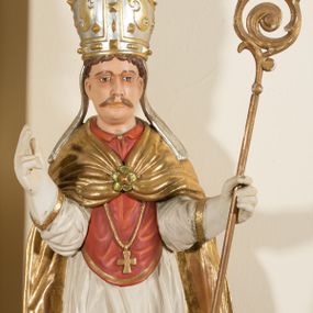Zdjęcie nr 1: Rzeźba ścięta z tyłu, przedstawia św. Stanisława. Święty ukazany w postawie stojącej na niskim cokole, frontalnie, w statycznej pozie, z rękami wyciągniętymi do przodu i odwiedzionymi delikatnie na boki: prawą wykonuje gest błogosławieństwa, w lewej trzyma pastorał. Ma szeroką twarz, z długim i prostym nosem, wzrokiem skierowanym na wprost oraz wąsy. Włosy krótkie, kędzierzawe, ciemnobrązowe. Święty jest ubrany jest w czerwoną sutannę, białą rokietę zdobioną na brzegach złoceniem, czerwony mucet, złotą kapę, spiętą na piersiach broszą, białe rękawice, jasnobrązowe buty oraz srebrzoną infułę, zdobioną złoconymi kaboszonami, rautami, motywami w kształcie litery „S” oraz czteropłatkowymi kwiatami. Na piersi ma zawieszony złocony krzyż pektoralny. Obok jego prawej nogi znajduje się mała klęcząca postać Piotrowina ze złożonymi rękami, ubranego w białą, długą suknię i zielony płaszcz. Polichromia w odsłoniętych partiach ciała jest naturalistyczna. Cokół jasnozielony, z przodu czarno malowany napis: „ŚW(IĘTY) STANISŁAW.” 




