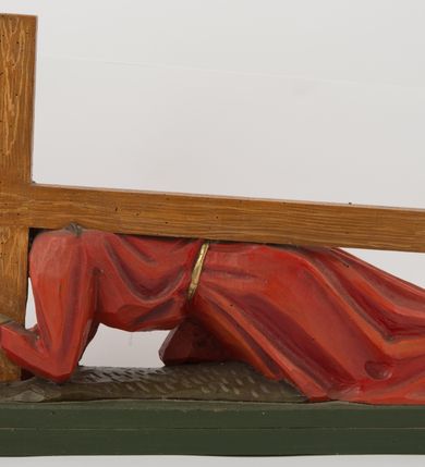 Zdjęcie nr 2: Pełnoplastyczna, wolnostojąca rzeźba Chrystusa upadającego pod krzyżem ustawiona na niskim, prostopadłościennym postumencie. Chrystus przedstawiony jest w pozycji półklęczącej, z prawą nogą ugiętą w kolanie, wysuniętą do przodu, lewą wyprostowaną do tyłu, z ciałem podpartym na ugiętym w łokciu prawym ramieniu. Lewą ręką podtrzymuje krzyż. Twarz pociągła, okolona ciemnym zarostem oraz długimi opadającymi na plecy i ramiona włosami. Chrystus jest ubrany w długą, czerwoną szatę przepasaną złotym sznurem. Na głowie złocona cierniowa korona. Figura w pełni polichromowana.