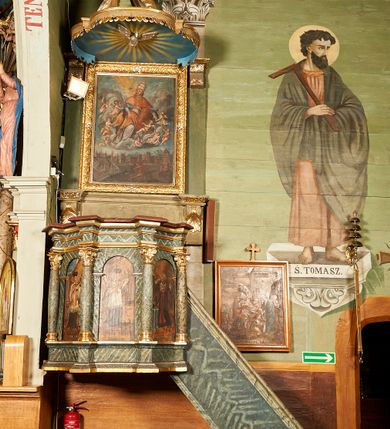 Zdjęcie nr 1: Ambona wisząca, przyścienna. Kosz na planie ośmioboku, na ściankach arkady z malowanymi przedstawieniami św. Walentego, św. Wincentego, św. Jana Nepomucena i bł. Jana Kanonika. Ścianki wydzielone kolumnami kompozytowymi na cokole, dźwigającymi pełne belkowanie wyłamane na ich osi. Parapet w formie silnie wystającego, profilowanego gzymsu. Z prawej strony dostawione jednobiegowe schody z barierką zwieńczoną profilowanym gzymsem. Zaplecek wysoki, ujęty pilastrami dźwiganymi przez konsolki dekorowane liściem; w polu obraz św. Grzegorza Wielkiego. Baldachim na planie trójliścia z lambrekinem z ornamentu roślinnego; utworzony z czterech pałąków dekorowanych akantem, podtrzymujących cokół dla figury św. Michała Archanioła. Figura zwrócona frontalnie, z prawą nogą opartą na fragmencie skały. W lewej ręce trzyma włócznię, w prawej miecz. Ubrany w zbroję, z szeroko rozłożonymi skrzydłami. Na podniebieniu gołębica Ducha Świętego na tle glorii promienistej. Ambona marmoryzowana w tonacji zielono-niebieskiej ze złoconymi detalami i ornamentami.
św. Jana Kantego, św. Jana Nepomucena, św. Walentego i św. Wincentego

św. grzegorz unoszący się nad rzymem