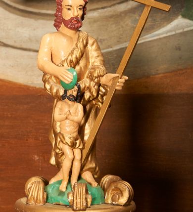 Zdjęcie nr 3: Chrzcielnica ustawiona podstawie z uskokiem. Trzon tworzy gruszkowaty nodus z pierścieniem. Czara puklowana, o wywiniętym wylewie. Pokrywa na planie koła, przechodząca w sześciobok ze ścianami dekorowanymi uskrzydlonymi główkami anielskimi. Na niej ustawiono sześć pałąków zdobionych wolutowo skręconymi liśćmi akantu, dźwigających podstawę dla grupy rzeźbiarskiej z przedstawieniem chrztu Chrystusa. Frontalnie ustawiony Jan Chrzciciel jest ubrany w melotę, w lewej ręce trzyma krzyż, w prawej przechyloną misę. Przed nim nieproporcjonalnie mała postać Chrystusa w kontrapoście, z dłońmi złożonymi w geście modlitwy.