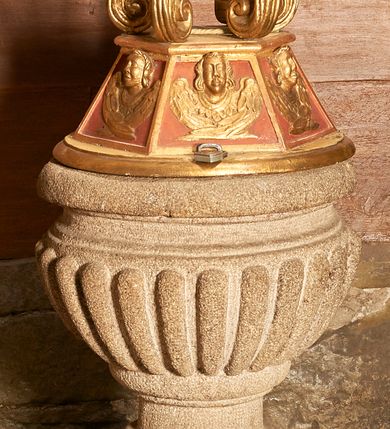 Zdjęcie nr 1: Chrzcielnica ustawiona podstawie z uskokiem. Trzon tworzy gruszkowaty nodus z pierścieniem. Czara puklowana, o wywiniętym wylewie. Pokrywa na planie koła, przechodząca w sześciobok ze ścianami dekorowanymi uskrzydlonymi główkami anielskimi. Na niej ustawiono sześć pałąków zdobionych wolutowo skręconymi liśćmi akantu, dźwigających podstawę dla grupy rzeźbiarskiej z przedstawieniem chrztu Chrystusa. Frontalnie ustawiony Jan Chrzciciel jest ubrany w melotę, w lewej ręce trzyma krzyż, w prawej przechyloną misę. Przed nim nieproporcjonalnie mała postać Chrystusa w kontrapoście, z dłońmi złożonymi w geście modlitwy.