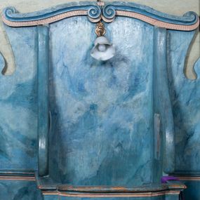 Zdjęcie nr 1: Drewniany konfesjonał ustawiony na jednostopniowym podwyższeniu na rzucie półkolistym. Drzwiczki wypukłe, dekorowane u góry przestylizowanym lambrekinem. Boki ujęte spływami wolutowymi. Zaplecek zamknięty dwiema przeciwstawnie ustawionymi wolutami. Struktura marmoryzowana na kolor niebieski z beżowymi elementami.