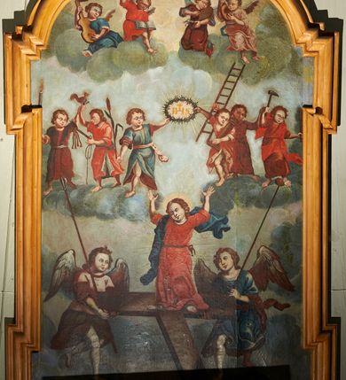 Zdjęcie nr 3: Obraz o kształcie prostokąta stojącego z uszakami w narożach, zamknięty od góry łukiem nadwieszonym. W dolnej części dwóch aniołów z włóczniami trzyma drewniany krzyż w kształcie litery T. Na nim stoi w kontrapoście triumfujący Chrystus z uniesionymi rękami i głową przechyloną na prawe ramię. Ma młodą, owalna twarz, ciemne oczy, prosty nos i pełne usta; wokół głowy świetlisty nimb. Jest ubrany w czerwoną tunikę przepasaną cigulum, a błękitny płaszcz przechodzący przez prawy bark rozwiewa się za jego sylwetką. W górnej części przedstawiono grupy aniołów unoszące się na obłokach. Dwa w centrum kompozycji podtrzymują nad głową Chrystusa koronę cierniową z wpisanym w nią monogramem „IHS”. Po ich bokach, bliżej krawędzi obrazu dwie grupy po dwa anioły w dynamicznych pozach prezentują Arma Christi. W podłuczu cztery anioły pogrupowane na dwóch obłokach przygrywają na instrumentach muzycznych. Jeden z nich, ubrany w czerwoną tunikę ma na kolanach otwartą księgę, a prawą rękę unosi wysoko. Tło obrazu stanowią szarobłękitne obłoki. U góry przebijają się promienie ciepłego słonecznego światła. Rama drewniana, profilowana, pomalowana na kolor jasnobrązowy.