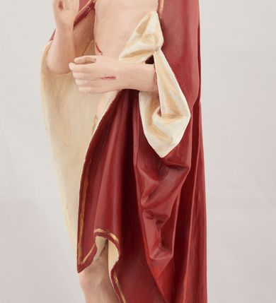 Zdjęcie nr 3: Rzeźba pełnoplastyczna przedstawiająca stojącego Chrystusa Zmartwychwstałego ustawiona na zielonej, owalnej podstawie i profilowanym, sześciobocznym cokoliku. Głowa zwrócona na wprost, twarz wydłużona, wzrok skierowany przed siebie, nos długi prosty, usta pełne. Twarz okala krótki brązowy zarost, włosy brązowe opadające na ramiona. Prawa ręka uniesiona w geście błogosławieństwa, lewa ugięta w łokciu na wysokość pasa, palce złączone. Na rękach, stopach i piersi widoczne ślady męczeństwa. Stopy nagie, biodra otacza złote, płasko sfałdowane perizonium. Płaszcz ciemnoczerwony ze złotą lamówką i białym podbiciem, rzeźbiony w głębokie fałdy. 