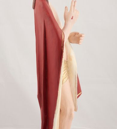 Zdjęcie nr 6: Rzeźba pełnoplastyczna przedstawiająca stojącego Chrystusa Zmartwychwstałego ustawiona na zielonej, owalnej podstawie i profilowanym, sześciobocznym cokoliku. Głowa zwrócona na wprost, twarz wydłużona, wzrok skierowany przed siebie, nos długi prosty, usta pełne. Twarz okala krótki brązowy zarost, włosy brązowe opadające na ramiona. Prawa ręka uniesiona w geście błogosławieństwa, lewa ugięta w łokciu na wysokość pasa, palce złączone. Na rękach, stopach i piersi widoczne ślady męczeństwa. Stopy nagie, biodra otacza złote, płasko sfałdowane perizonium. Płaszcz ciemnoczerwony ze złotą lamówką i białym podbiciem, rzeźbiony w głębokie fałdy. 