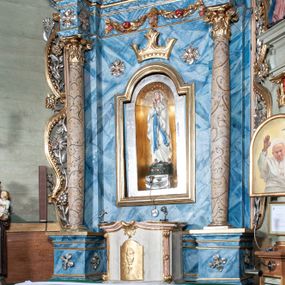 Zdjęcie nr 1: Ołtarz przyścienny, architektoniczny, jednoosiowy, jednokondygnacyjny ze zwieńczeniem i ażurowymi uszakami o falistym brzegu. Mensa prostopadłościenna z portatylem, antepedium ujęte profilowanymi listwami z polem wewnętrznym dekorowanym silnie stylizowanym, malowanym ornamentem o esowatym przebiegu i wolutowych końcach. Na mensie tabernakulum prostopadłościenne, na planie wklęsło-wypukłym, ujęte na narożach taśmami o skręconych końcach, zamknięte falującym gzymsem, pośrodku którego rocaille. Drzwiczki prostokątne, pozłacane z płaskorzeźbionym kielichem z hostią, zamknięte łukiem nadwieszonym. Tabernakulum marmoryzowane na jasnokremowy odcień. Retabulum ujęte parą kolumn kompozytowych ustawionych na niskich cokołach z rozetką, wspierających belkowanie wyłamujące się ponad nimi, z wydatnym, profilowanym gzymsem. Fryz dekorowany girlandami kwiatów w części środkowej, po bokach rozetkami. Nad belkowaniem na osiach kolumn ustawione wazony o żłobionej w dwóch strefach powierzchni. Pole środkowe z niszą ujętą prostokątną, profilowaną ramą, zamkniętą łukiem nadwieszonym. W niszy figura Matki Boskiej z Lourdes. Nad łukiem pozłacana korona otwarta i rozetki. Zwieńczenie półkoliste, ujęte spływami wolutowymi, na których rzeźby uskrzydlonych aniołków. Pośrodku zwieńczenia owalny obraz z przedstawieniem św. Józefa z Dzieciątkiem ujęty ramą uformowaną z obłoków z odchodzącymi promieniami. Nad zwieńczeniem rzeźbiona, złocona korona zamknięta. Całość struktury ołtarza marmoryzowana na kolor niebieski z ciemniejszymi żyłkami; kolumny jasnobrązowe z malowaną z wicią roślinną; ornamenty i profile złocone i srebrzone. 