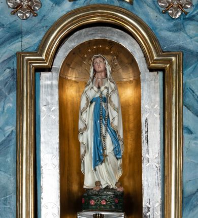 Zdjęcie nr 3: Ołtarz przyścienny, architektoniczny, jednoosiowy, jednokondygnacyjny ze zwieńczeniem i ażurowymi uszakami o falistym brzegu. Mensa prostopadłościenna z portatylem, antepedium ujęte profilowanymi listwami z polem wewnętrznym dekorowanym silnie stylizowanym, malowanym ornamentem o esowatym przebiegu i wolutowych końcach. Na mensie tabernakulum prostopadłościenne, na planie wklęsło-wypukłym, ujęte na narożach taśmami o skręconych końcach, zamknięte falującym gzymsem, pośrodku którego rocaille. Drzwiczki prostokątne, pozłacane z płaskorzeźbionym kielichem z hostią, zamknięte łukiem nadwieszonym. Tabernakulum marmoryzowane na jasnokremowy odcień. Retabulum ujęte parą kolumn kompozytowych ustawionych na niskich cokołach z rozetką, wspierających belkowanie wyłamujące się ponad nimi, z wydatnym, profilowanym gzymsem. Fryz dekorowany girlandami kwiatów w części środkowej, po bokach rozetkami. Nad belkowaniem na osiach kolumn ustawione wazony o żłobionej w dwóch strefach powierzchni. Pole środkowe z niszą ujętą prostokątną, profilowaną ramą, zamkniętą łukiem nadwieszonym. W niszy figura Matki Boskiej z Lourdes. Nad łukiem pozłacana korona otwarta i rozetki. Zwieńczenie półkoliste, ujęte spływami wolutowymi, na których rzeźby uskrzydlonych aniołków. Pośrodku zwieńczenia owalny obraz z przedstawieniem św. Józefa z Dzieciątkiem ujęty ramą uformowaną z obłoków z odchodzącymi promieniami. Nad zwieńczeniem rzeźbiona, złocona korona zamknięta. Całość struktury ołtarza marmoryzowana na kolor niebieski z ciemniejszymi żyłkami; kolumny jasnobrązowe z malowaną z wicią roślinną; ornamenty i profile złocone i srebrzone. 