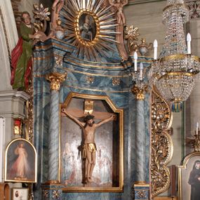 Zdjęcie nr 1: Ołtarz przyścienny, architektoniczny, jednoosiowy, jednokondygnacyjny ze zwieńczeniem i ażurowymi uszakami o falistym brzegu. Mensa w typie sarkofagowym, profilowana, z kamiennym portatylem. Retabulum wklęsłe, ujęte parą kolumn kompozytowych ustawionych na kostkowych cokołach z rozetkami, wspierających belkowanie wyłamujące się ponad nimi, zamknięte wydatnym, profilowanym gzymsem. Fryz dekorowany rozetkami. Nad belkowaniem na osiach kolumn ustawione wazony o marmoryzowanej i żłobionej powierzchni. W polu środkowym głęboka wnęka zamknięta wielobocznie, w której rzeźbiony krucyfiks, po jego bokach malowane postacie Matki Boskiej i Św. Jana na tle pejzażu z architekturą. Zwieńczenie półkoliste ujęte spływami wolutowymi, na których rzeźby aniołków z arma Christi (aniołek po prawej z włócznią, po lewej zaś z gąbką). Pośrodku zwieńczenia owalny obraz z przedstawieniem św. Wojciecha ujęty ramą uformowaną z obłoków z odchodzącymi promieniami. Nad zwieńczeniem rzeźbiona, złocona korona zamknięta. Struktura ołtarza polichromowana, marmoryzowana na odcień niebieski, antepedium z polem marmoryzowanym na kolor beżowy. 