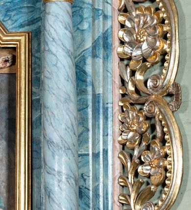 Zdjęcie nr 6: Ołtarz przyścienny, architektoniczny, jednoosiowy, jednokondygnacyjny ze zwieńczeniem i ażurowymi uszakami o falistym brzegu. Mensa w typie sarkofagowym, profilowana, z kamiennym portatylem. Retabulum wklęsłe, ujęte parą kolumn kompozytowych ustawionych na kostkowych cokołach z rozetkami, wspierających belkowanie wyłamujące się ponad nimi, zamknięte wydatnym, profilowanym gzymsem. Fryz dekorowany rozetkami. Nad belkowaniem na osiach kolumn ustawione wazony o marmoryzowanej i żłobionej powierzchni. W polu środkowym głęboka wnęka zamknięta wielobocznie, w której rzeźbiony krucyfiks, po jego bokach malowane postacie Matki Boskiej i Św. Jana na tle pejzażu z architekturą. Zwieńczenie półkoliste ujęte spływami wolutowymi, na których rzeźby aniołków z arma Christi (aniołek po prawej z włócznią, po lewej zaś z gąbką). Pośrodku zwieńczenia owalny obraz z przedstawieniem św. Wojciecha ujęty ramą uformowaną z obłoków z odchodzącymi promieniami. Nad zwieńczeniem rzeźbiona, złocona korona zamknięta. Struktura ołtarza polichromowana, marmoryzowana na odcień niebieski, antepedium z polem marmoryzowanym na kolor beżowy. 