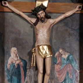 Zdjęcie nr 1: Rzeźba pełnoplastyczna, ścięta w partii pleców, polichromowana figura Chrystusa na prostym krzyżu, przybita do niego trzema metalowymi gwoździami. Sylwetka zmarłego Jezusa jest smukła, wychudzona, z wyraźnie zarysowaną klatką piersiową. Ramiona rozpostarte, uniesione ponad głowę. Nogi z zaznaczonym zarysem mięśni są lekko ugięte w kolanach. Głowa opadająca, przechylona w prawą stronę, z szeroką koroną cierniową o gęstym splocie. Twarz pociągła z krótkim zarostem, oczy zamknięte, nos spiczasty o prostym profilu, usta otwarte, o opadłych kącikach. Włosy długie, rzeźbione w formie sznurów opadają na plecy i prawe ramię. Perizonium krótkie, okrywające górną część nóg, udrapowane na pojedynczym sznurze, fałdy płasko modelowane, zachodzące na siebie. Nad głową Zbawiciela pozłacany titulus z napisem „INRI”. Figura zmarłego Chrystusa pokryta polichromią imitującą naturalną karnację, ciemnoczerwoną farbą zaznaczone ślady męki na dłoniach, stopach, prawym boku i głowie. Perizonium pozłacane, włosy i zarost ciemnobrązowe, korona cierniowa czarna. Krucyfiks umieszczono na tle obrazu z przedstawieniem stojących pod krzyżem postaci Marii po lewej i św. Jana po prawej stronie. Maria stoi wyprostowana, spogląda na Jezusa, ręce składa na piersi. Ma pogodną, owalną twarz, duże oczy i prosty nos. Jest ubrana w różową suknię i bardzo obszerny niebieski płaszcz, który okrywa jej lewe ramię, plecy i prawą nogę, łamiąc się w grube fałdy. Na głowie ma biały welon, spod sukni wystają stopy w sandałach. Święty Jan stoi w wykroku, z prawą nogą z przodu. Lewą rękę ma odwiedzioną do tyłu, prawą przykłada do twarzy fragment płaszcza. Ma małą głowę, jasne długie włosy opadają mu na plecy. Jest ubrany w zieloną, przewiązaną w pasie suknię i czerwony płaszcz przytroczony przy lewym biodrze. Postacie stoją na tle widocznej w oddali panoramy miasta, reszta tła brunatna. 