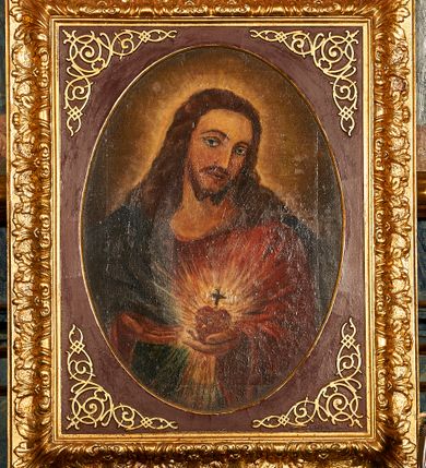 Zdjęcie nr 1: Obraz z przedstawieniem Najświętszego Serca Jezusa ukazanego w półpostaci, frontalnie z głową przechyloną w stronę lewego barku, sercem w lewej dłoni i wskazujący na nie prawą dłonią. Głowa zwrócona delikatnie w lewo, wzrok skierowany na widza, nos prosty, usta wąskie. Twarz okala bujny, ciemnobrązowy zarost, falowane włosy opadają na ramiona i plecy. Wokół głowy znajduje się świetlisty nimb. Chrystus ubrany jest w czerwoną suknię z długimi rękawami i granatowy płaszcz, który przerzucony ma przez prawy bark. Trzymane w dłoni serce jest otoczone koroną cierniową i zwieńczone krzyżem łacińskim, otacza je jasna, promienista gloria. Tło ciemnobrązowe, jaśniejące wokół głowy Chrystusa. Obraz ujęty jest w bogato zdobione prostokątne i profilowane ramy o owalnym świetle, dekorowane w narożach stylizowanym ornamentem cęgowym.