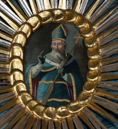 Zdjęcie nr 1: Obraz w kształcie owalu przedstawiający św. Wojciecha ukazanego w pozycji stojącej, w ujęciu do kolan, frontalnie, z prawą ręką uniesioną w geście błogosławieństwa, a lewą ręką trzymającą wiosło i ferulę – pastorał zakończony krzyżem. Twarz pociągła o wyrazistych kościach policzkowych, okolona siwymi włosami i długą, siwą, rozdwojoną brodą. Oczy migdałowate, brwi wyraziste, nos prosty, usta lekko otwarte. Święty jest ubrany w szaty biskupie: niebieską, poprzecinaną złotymi pasami sutannę i lamowany złotem płaszcz podbity purpurą, niebieskie rękawiczki, paliusz oraz infułę.