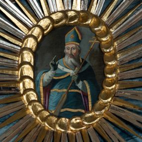 Zdjęcie nr 1: Obraz w kształcie owalu przedstawiający św. Wojciecha ukazanego w pozycji stojącej, w ujęciu do kolan, frontalnie, z prawą ręką uniesioną w geście błogosławieństwa, a lewą ręką trzymającą wiosło i ferulę – pastorał zakończony krzyżem. Twarz pociągła o wyrazistych kościach policzkowych, okolona siwymi włosami i długą, siwą, rozdwojoną brodą. Oczy migdałowate, brwi wyraziste, nos prosty, usta lekko otwarte. Święty jest ubrany w szaty biskupie: niebieską, poprzecinaną złotymi pasami sutannę i lamowany złotem płaszcz podbity purpurą, niebieskie rękawiczki, paliusz oraz infułę.