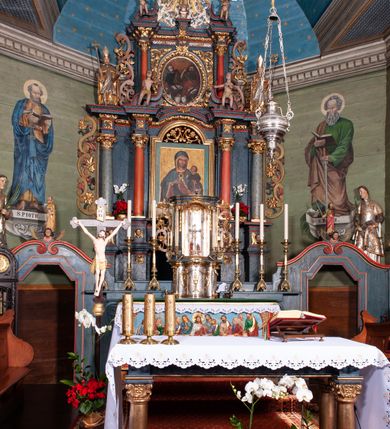 Zdjęcie nr 2: Nastawa ołtarzowa architektoniczna, dwukondygnacyjna, z bramkami, na podwójnym cokole. Pierwsza kondygnacja trójosiowa, ujęta dwiema parami kolumn o kapitelach korynckich, dźwigających pełne belkowanie wyłamane na ich osi i przerwane w partii pola środkowego, nad którym gzyms przyjmuje formę łuku odcinkowego. Na osi środkowych kolumn przerwany, falisty przyczółek. Pole obrazowe w formie stojącego prostokąta zamkniętego łukiem nadwieszonym, w nim obraz Matki Boskiej z Dzieciątkiem (na zasuwie Matki Boskiej Niepokalanie Poczętej) w profilowanej ramie; w podłuczu stylizowany, dekorowany kwiatami monogram Maryjny; u spodu lambrekin. Druga kondygnacja jednoosiowa, ujęta parą kolumn o kapitelach korynckich, dźwigających pełne belkowanie wyłamane wielokrotnie na ich osi oraz przerwany, falisty przyczółek. W drugiej kondygnacji obraz św. Piotra i św. Pawła w ramie dekorowanej stylizowanym akantem z elementami małżowiny oraz wieńcem; zwieńczonej rozetą z liśćmi akantu. Pole obrazowe ujęte suchym akantem oraz parą festonów z owocami.  Zwieńczenie w kształcie glorii promienistej z gołębicą Ducha Świętego na tle obłoków. Cokół dekorowany uskrzydlonymi główkami anielskimi i akantem. Fryz zdobiony rozetami i suchym akantem oraz pasem akantu z elementami małżowiny. Pierwsza kondygnacja ujęta uszami w formie wolut z elementami roślinnymi i kwiatami. Na przerwanym przyczółku siedząca para puttów; na gzymsie figury św. Wojciecha i św. Stanisława biskupa. Fryz dekorowany ornamentem roślinnym oraz pasem akantu z elementami małżowiny na osi kolumn oraz rozetami w centrum. Druga kondygnacja ujęta uszami w formie cęgów przeplatanych gałązką różaną. Na gzymsie w centrum postument zdobiony winną latoroślą, na nim wazon z elementami roślinnymi. Na przerwanym przyczółku para puttów. Podstawę dla glorii tworzy suchy akant.  Ołtarz z kamienną mensą. Antepedium w formie ramy z płaskorzeźbionym przedstawieniem Ostatniej Wieczerzy. Ołtarz w drewnianej obudowie, ujęty spływami wolutowymi dekorowanymi kogucim grzebieniem, zakończony podwójnym parapetem. Tabernakulum o falistej, wypukłej ścianie frontowej; ujęte pilastrami w formie spływów wolutowych dekorowanych kogucim grzebieniem, dźwigającymi profilowany gzyms, wyłamany na ich osi z palmetą w centrum. Drzwiczki w formie stojącego prostokąta zamkniętego łukiem nadwieszonym z apliką w postaci kielicha z hostią w glorii; ujęte rocaille'm. Tron wystawienia w formie niszy flankowanej kolumnami na cokołach o żłobkowanych trzonach, dźwigających imposty. Całość zamknięta wybrzuszonym gzymsem. W konsze rozeta w otoczeniu liści. Tron ujęty uszami w postaci cęgów przeplatanych gałązkami różanymi. Po bokach ołtarza bramki zamknięte przeciwstawnie zwróconymi wolutami dekorowanymi uskrzydlonymi główkami anielskimi. Przejścia w formie prostokąta zamkniętego trójbocznie, dekorowanego podwójną listewką; na końcach bramek dwie figury św. Wawrzyńca i św. Szczepana.
 Nastawa marmoryzowana na kolor niebieski, z czerwonymi elementami oraz złoconymi i srebrzonymi detalami architektonicznymi i ornamentyką; tabernakulum złocone i srebrzone, miejscami marmoryzowane na kolor niebieski; kolumienki szare. 