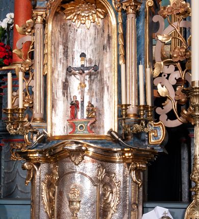 Zdjęcie nr 16: Nastawa ołtarzowa architektoniczna, dwukondygnacyjna, z bramkami, na podwójnym cokole. Pierwsza kondygnacja trójosiowa, ujęta dwiema parami kolumn o kapitelach korynckich, dźwigających pełne belkowanie wyłamane na ich osi i przerwane w partii pola środkowego, nad którym gzyms przyjmuje formę łuku odcinkowego. Na osi środkowych kolumn przerwany, falisty przyczółek. Pole obrazowe w formie stojącego prostokąta zamkniętego łukiem nadwieszonym, w nim obraz Matki Boskiej z Dzieciątkiem (na zasuwie Matki Boskiej Niepokalanie Poczętej) w profilowanej ramie; w podłuczu stylizowany, dekorowany kwiatami monogram Maryjny; u spodu lambrekin. Druga kondygnacja jednoosiowa, ujęta parą kolumn o kapitelach korynckich, dźwigających pełne belkowanie wyłamane wielokrotnie na ich osi oraz przerwany, falisty przyczółek. W drugiej kondygnacji obraz św. Piotra i św. Pawła w ramie dekorowanej stylizowanym akantem z elementami małżowiny oraz wieńcem; zwieńczonej rozetą z liśćmi akantu. Pole obrazowe ujęte suchym akantem oraz parą festonów z owocami.  Zwieńczenie w kształcie glorii promienistej z gołębicą Ducha Świętego na tle obłoków. Cokół dekorowany uskrzydlonymi główkami anielskimi i akantem. Fryz zdobiony rozetami i suchym akantem oraz pasem akantu z elementami małżowiny. Pierwsza kondygnacja ujęta uszami w formie wolut z elementami roślinnymi i kwiatami. Na przerwanym przyczółku siedząca para puttów; na gzymsie figury św. Wojciecha i św. Stanisława biskupa. Fryz dekorowany ornamentem roślinnym oraz pasem akantu z elementami małżowiny na osi kolumn oraz rozetami w centrum. Druga kondygnacja ujęta uszami w formie cęgów przeplatanych gałązką różaną. Na gzymsie w centrum postument zdobiony winną latoroślą, na nim wazon z elementami roślinnymi. Na przerwanym przyczółku para puttów. Podstawę dla glorii tworzy suchy akant.  Ołtarz z kamienną mensą. Antepedium w formie ramy z płaskorzeźbionym przedstawieniem Ostatniej Wieczerzy. Ołtarz w drewnianej obudowie, ujęty spływami wolutowymi dekorowanymi kogucim grzebieniem, zakończony podwójnym parapetem. Tabernakulum o falistej, wypukłej ścianie frontowej; ujęte pilastrami w formie spływów wolutowych dekorowanych kogucim grzebieniem, dźwigającymi profilowany gzyms, wyłamany na ich osi z palmetą w centrum. Drzwiczki w formie stojącego prostokąta zamkniętego łukiem nadwieszonym z apliką w postaci kielicha z hostią w glorii; ujęte rocaille&#039;m. Tron wystawienia w formie niszy flankowanej kolumnami na cokołach o żłobkowanych trzonach, dźwigających imposty. Całość zamknięta wybrzuszonym gzymsem. W konsze rozeta w otoczeniu liści. Tron ujęty uszami w postaci cęgów przeplatanych gałązkami różanymi. Po bokach ołtarza bramki zamknięte przeciwstawnie zwróconymi wolutami dekorowanymi uskrzydlonymi główkami anielskimi. Przejścia w formie prostokąta zamkniętego trójbocznie, dekorowanego podwójną listewką; na końcach bramek dwie figury św. Wawrzyńca i św. Szczepana.
 Nastawa marmoryzowana na kolor niebieski, z czerwonymi elementami oraz złoconymi i srebrzonymi detalami architektonicznymi i ornamentyką; tabernakulum złocone i srebrzone, miejscami marmoryzowane na kolor niebieski; kolumienki szare. 