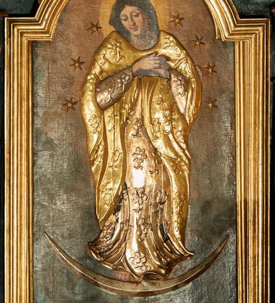 Zdjęcie nr 1: Obraz w kształcie stojącego prostokąta zamkniętego łukiem nadwieszonym w profilowanej, złoconej ramie. W centrum kompozycji ukazana Matka Boska w całej postaci, stojąca na półksiężycu z zaznaczonymi rysami twarzy oraz globie, depcząca węża trzymającego w paszczy jabłko. Obie ręce ma złożone na piersi, głowę skłania. Ma owalną, delikatną twarz, spogląda w dół, ma ciemne oczy przesłonięte dużymi powiekami, wąski nos i niewielkie usta oraz długie, ciemne włosy opadające na plecy. Jej głowę otacza świetlisty nimb, ramiona i głowę wieniec z 10 gwiazd. Ubranie jest przysłonięte płaskorzeźbioną, drewnianą sukienkę w postaci tuniki i płaszcza dekorowanych kwiatami, stopy bose. Tło ciemnobrązowe, niejednolite, kolorystyka ciepła, brunatna.