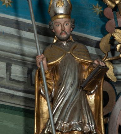 Zdjęcie nr 1: Rzeźba pełna, święty zwrócony na wprost, w kontrapoście. Lewą ręką podtrzymuje księgę opartą na biodrze, w prawej trzyma krzyż arcybiskupi. Twarz pociągła, o wyraźnych rysach, okolona zarostem; włosy krótkie, falowane. Święty jest ubrany w złotą albę, srebrną komżę dekorowaną u spodu ornamentem roślinnym oraz złotą kapę zapiętą na piersi fibulą; na głowie ma infułę. Polichromia naturalistyczna w partiach ciała.