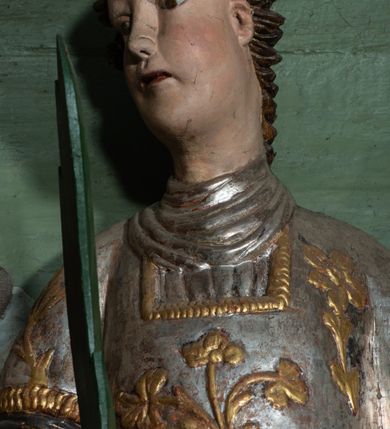 Zdjęcie nr 2: Rzeźba drążona, ścięta z tyłu. Figura zwrócona na wprost, z głową skręconą lekko w prawo. Ręce opuszczone na dół, w prawej zielona palma męczeństwa, w lewej szare kamienie. Twarz pełna, o małych oczach, długim nosie i wąskich ustach. Włosy krótkie, kręcone. Święty jest ubrany w szarą albę, srebrzoną u dołu z rękawami zakończonymi złotą lamówką, srebrny humerał oraz dalmatykę dekorowaną ukwieconymi gałązkami. Polichromia naturalistyczna w partiach ciała.